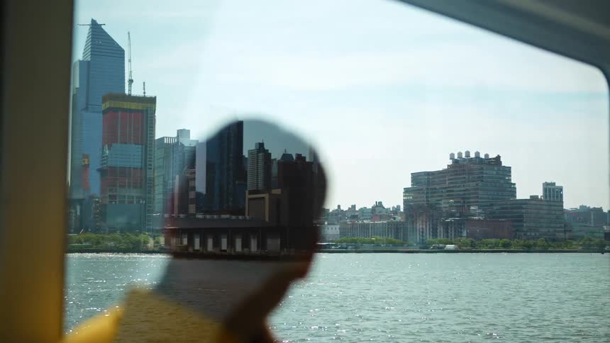 A male passenger watches big city skyline as traveling by a ferry across a river