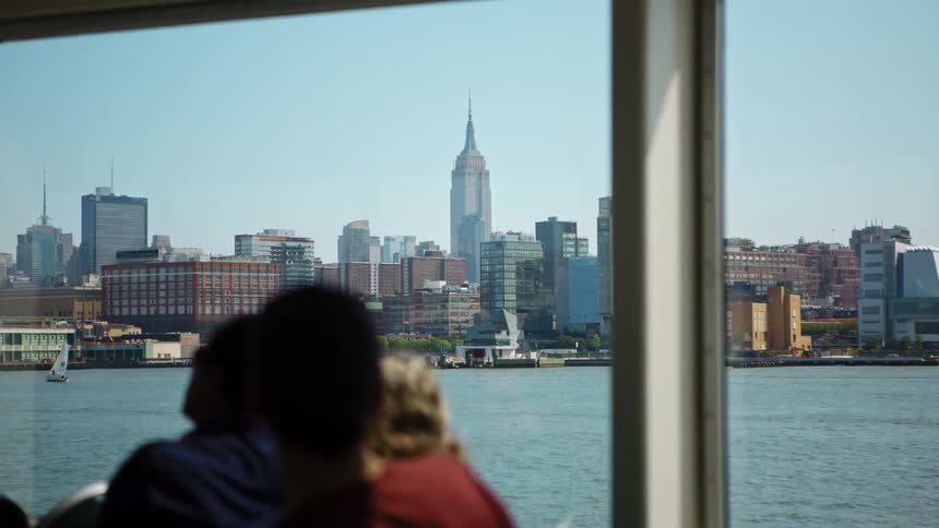 People sitting on a boat look out at the water a sailboat and the city skyline