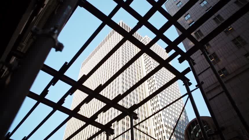 A tall skyscraper in a downtown area is seen through metal scaffolding