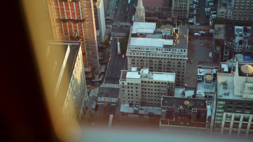 A window from a high rise building has views of a busy and dense neighborhood below