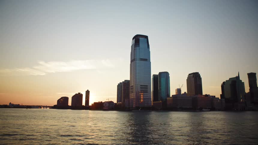 Big city skyline from a distant with multiple tall buildings seen from sea on the horizon at sunset