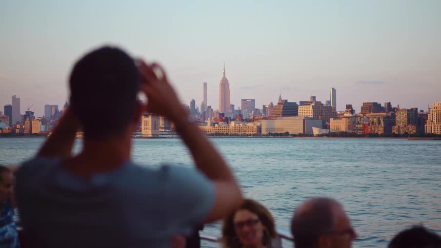 Man rides in a boat in a river and takes photos of the city buildings in the distance