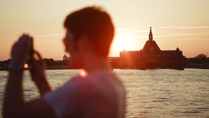 A man takes a picture of the landscape and water as boats drive past