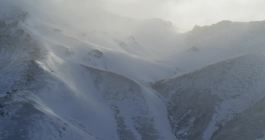 Clouds diffuse the sunset light over snowy mountains