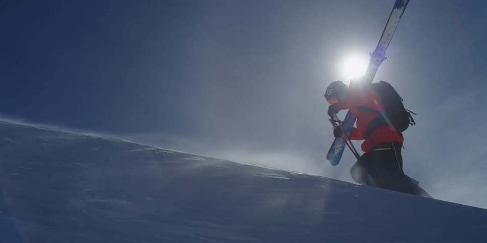Skier walks uphill through windblown snow
