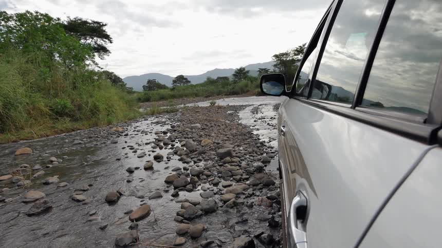 A vehicle driving through a shallow, rocky creek