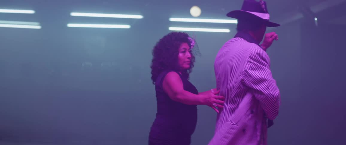 Man and woman dance on a hardwood floor illuminated by lights