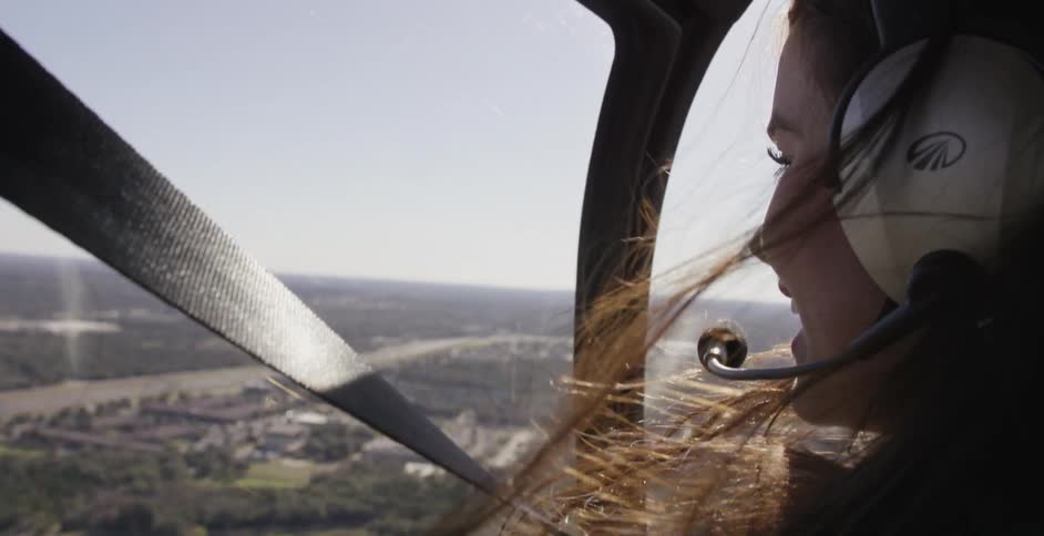A woman is smiling as she rides in an aircraft and looks down below