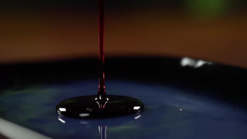 A viscous syrup like liquid is slowly drizzled onto a dark glass plate