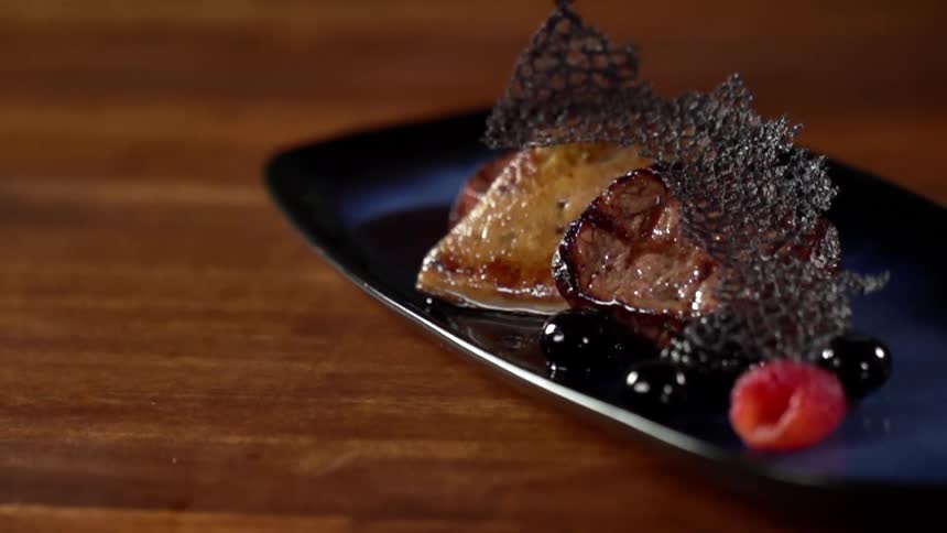 A meat dish with berries on the side sits on a wooden table