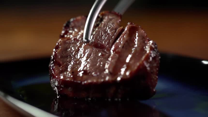 Cooked red meat steak placed on a ceramic blue plate with pliers