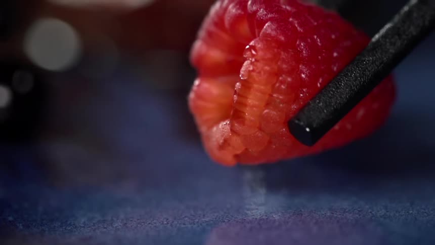 Metal tongs lower a red raspberry onto a counter top