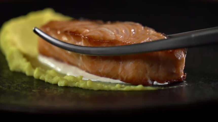 Tongs place a piece of meat onto lettuce on a plate