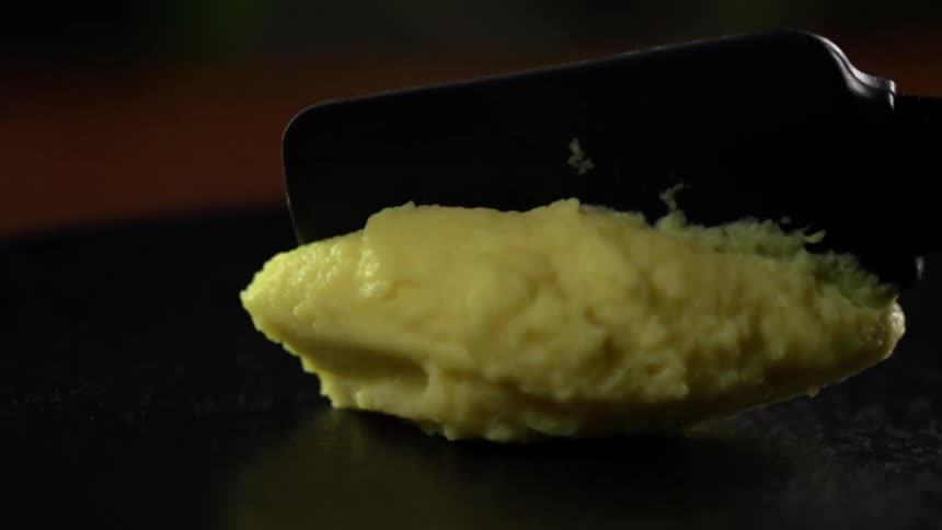 Batter is placed and flattened on a stone cooking surface with a black spatula