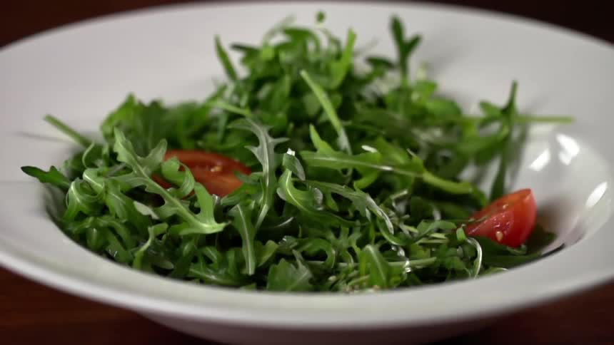 Tomatoes fall in to a bowl with arugula in it