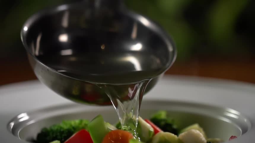 A ladle is pouring water over vegetables