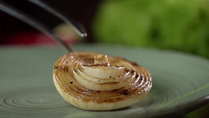 Slice of grilled onion placed in a ceramic dish using pliers