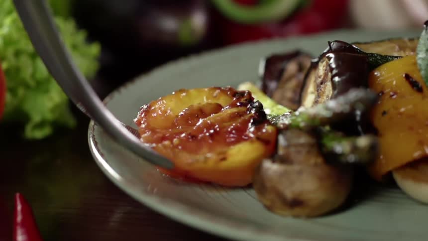 A grilled peach is placed on a plate with grilled vegetables