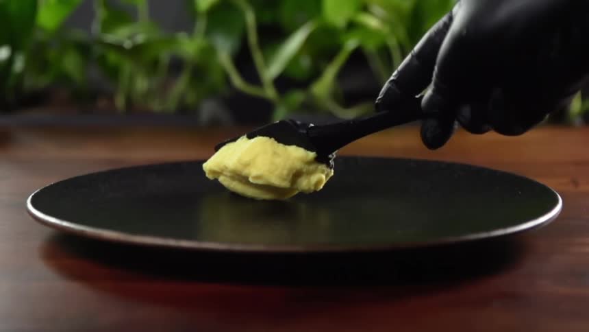 A black gloved hand smears food on a plate with a utensil