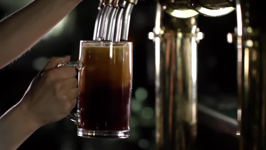 Person fills a big beer glass with dark beer from a beer tap