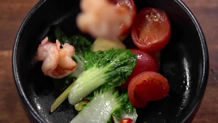 Vegetables and fried pork belly ina black ceramic bowl over a wooden table