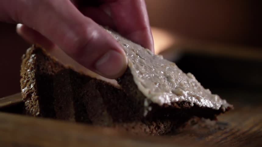 Hand picks up a slice of dark bread with cream on top from a wooden basket