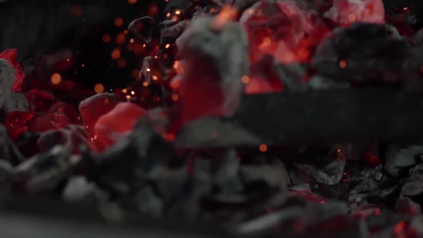 Coal being lifted with a shovel as gloves red from heat