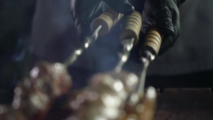 A person holds three skewers and while cooking the several pieces of steak on each one