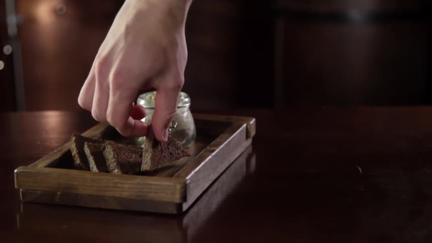 A hand picks up a piece of brown bread from a wooden tray