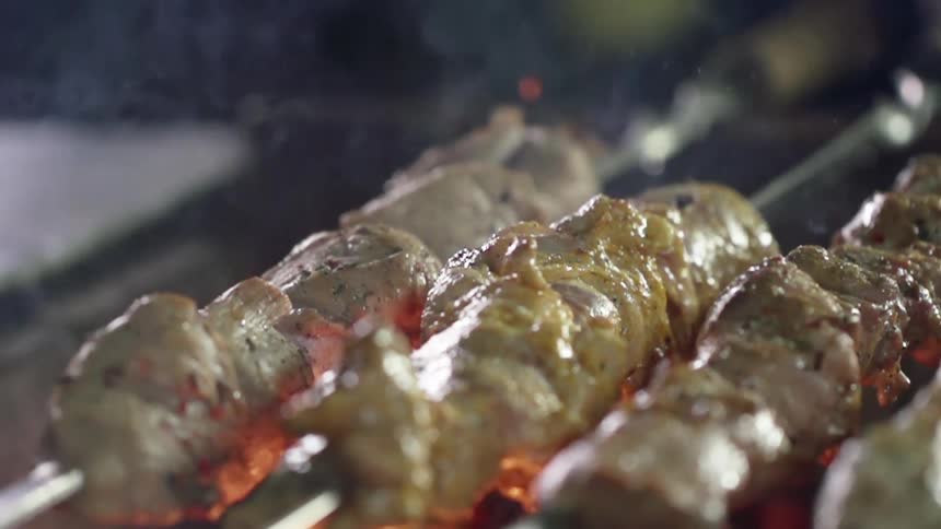 A meat skewer turns over a flame grill