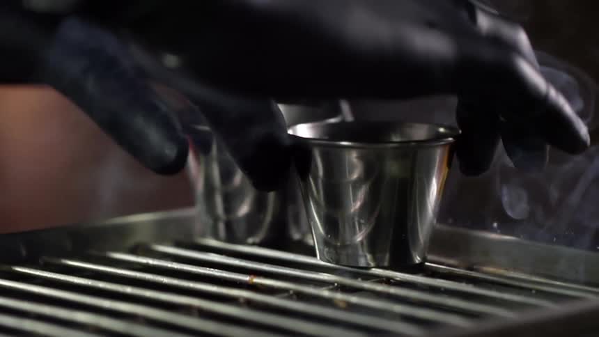 A person wearing black disposable gloves places two small metal cups atop a hot grill surface
