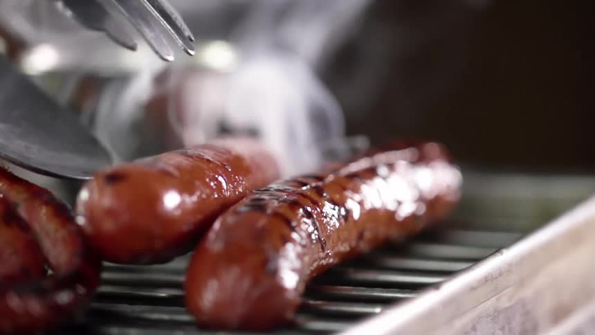 Sausages being moved with a pair of tongs as they are cooked on a steaming grill