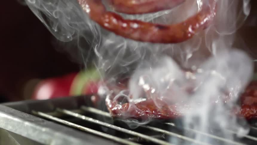A pair of tongs lowers a sausage to a hot grill