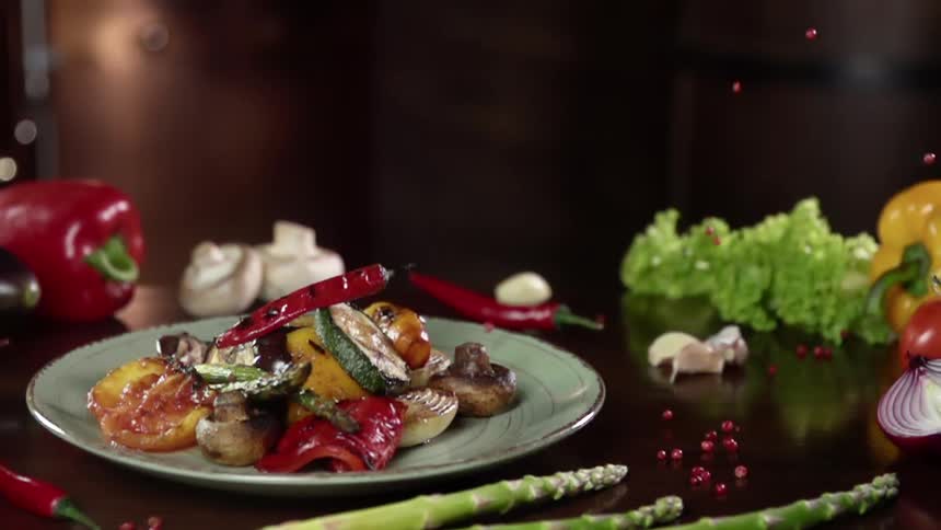 Red seeds fall to a table near a plate piled with cooked vegetables and mushroom
