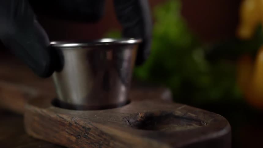 A person wearing black disposable gloves places a small stainless steel cup into a wooden carrier