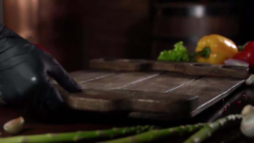 A person places a wooden try on a table amongst scattered vegetables