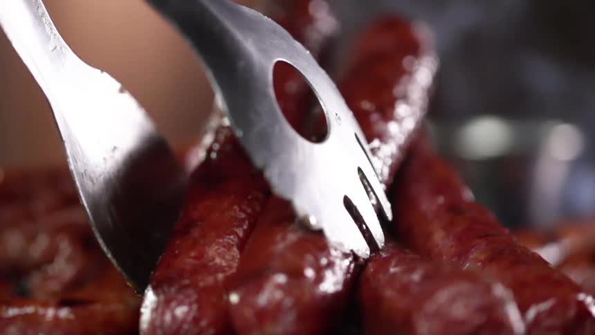 Close up of sausages being put on a plate by a pair of tongs