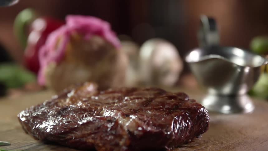 Metal tongs drop a cooked steak on a table