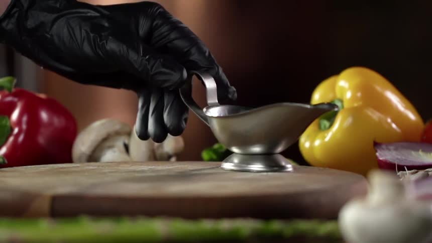 A person sets a gravy boat on a wood platter next to vegetables
