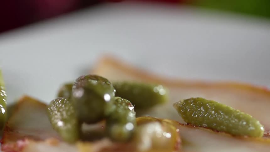 Small pickles fall over pieces of bacon in a white ceramic dish