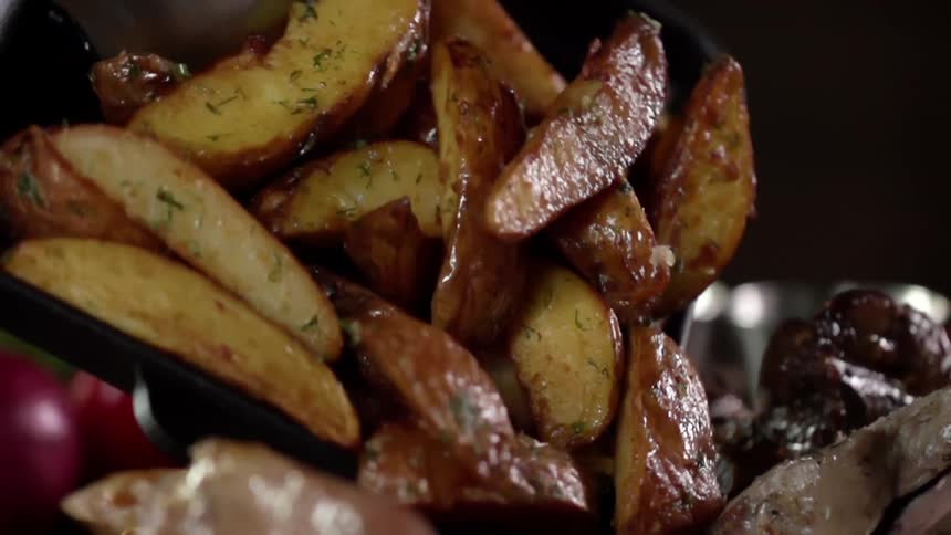 A tray full of delicious looking grilled potatoes is being poured onto a plate with other food