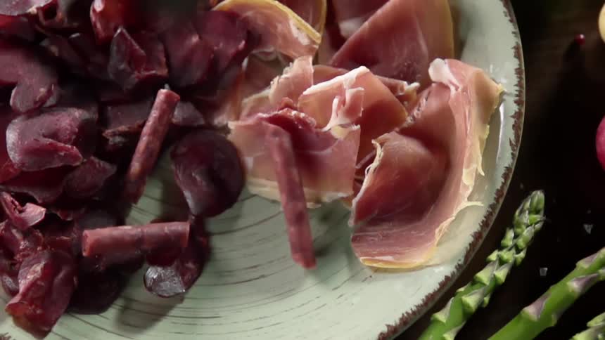 Sausage falling into a charcuterie plate filled with smoked and cured meats
