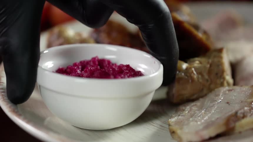 A person wearing a black glove sets a small bowl with red food in it down on a plate
