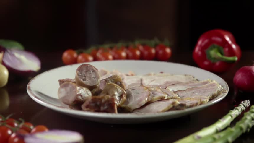 Chunks of sausage drop on a plate partially covered in slices of meat