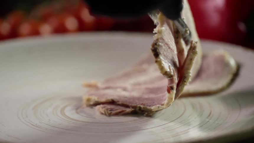 Metal tongs drop slices of meat on a plate