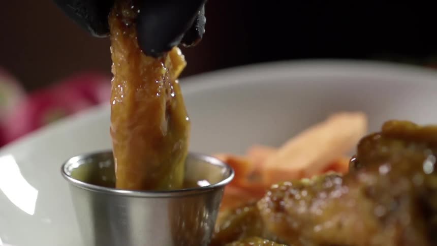 A gloved hand dips meat into a sauce