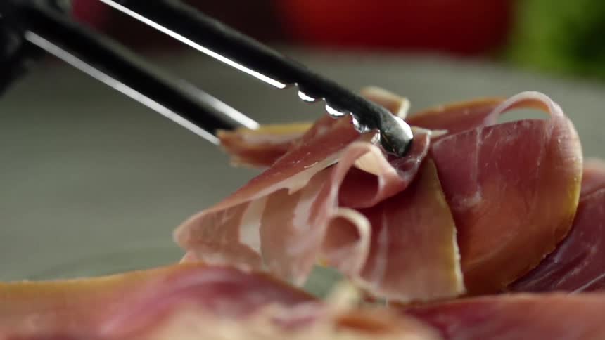 A person puts a slice of meat on a plate with metal tongs