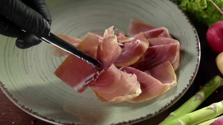 A person wearing a black glove piles sliced meat on a plate