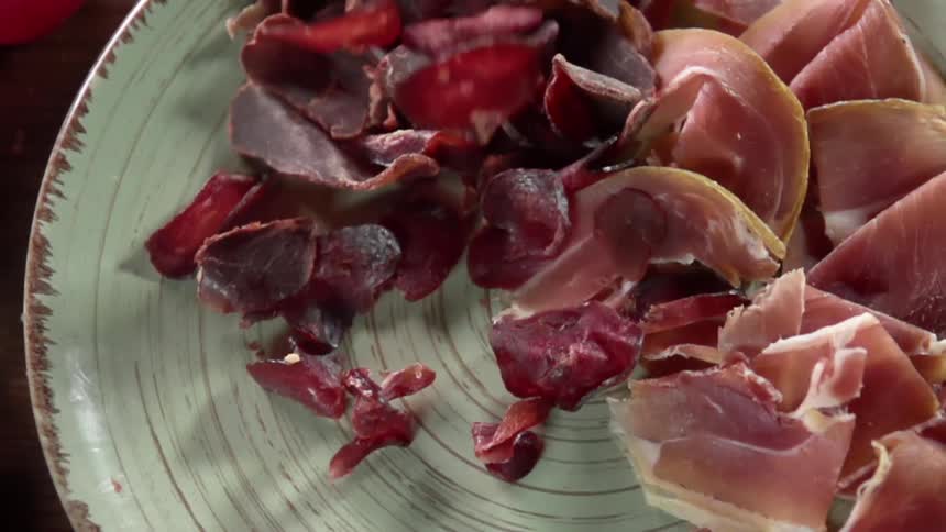 Pepperoni slices falling onto a plate of sliced meat