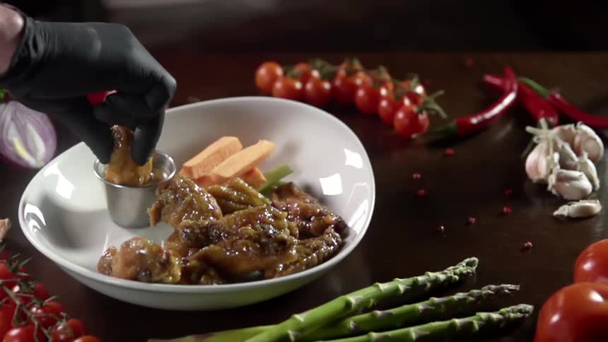 Chef wearing black latex gloves dips chicken nugget in sauce